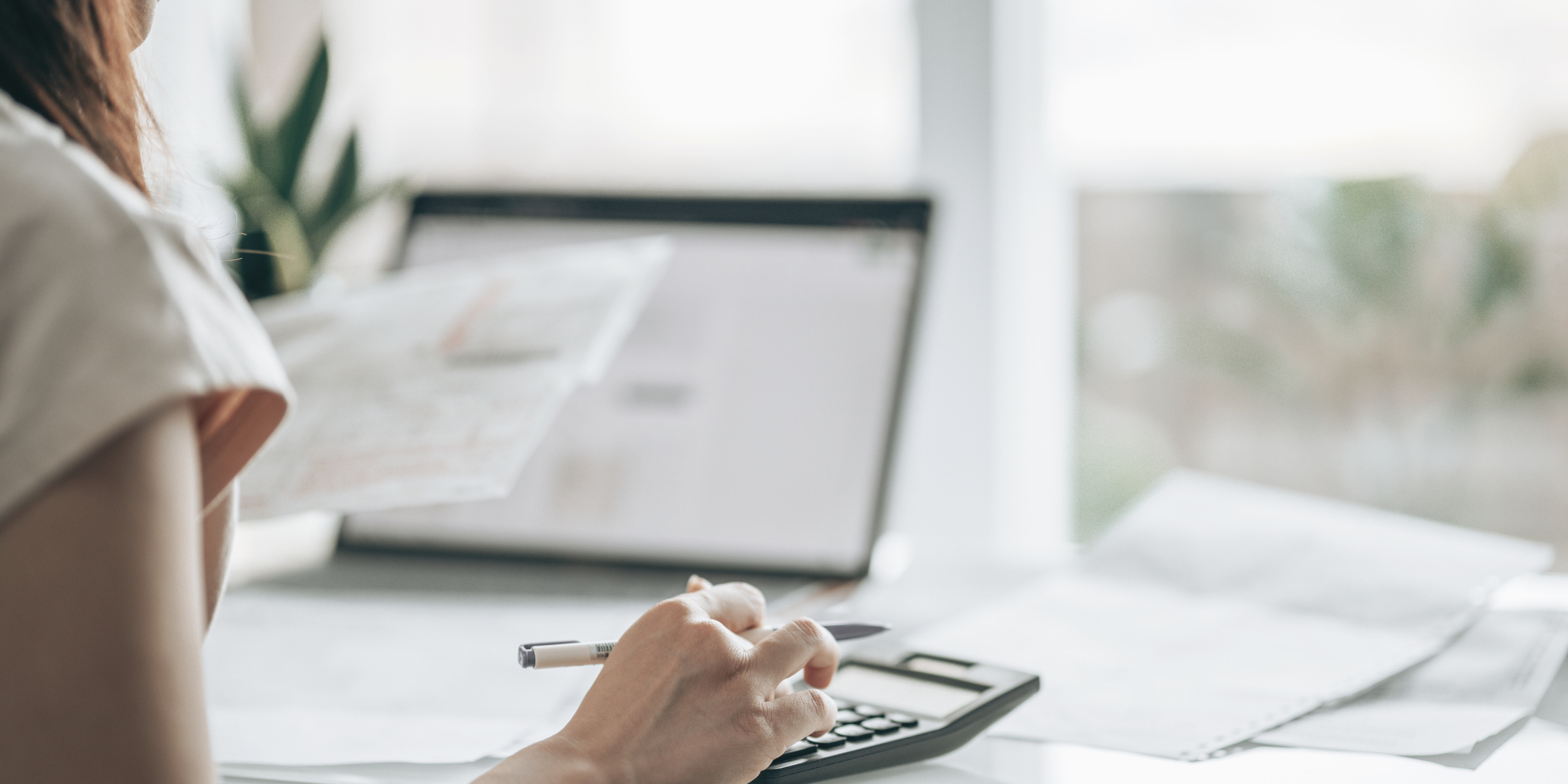 een persoon werkt met een pen en rekenmachine, naast papieren en een open laptop op een bureau een persoon werkt met een pen en rekenmachine, naast papieren en een open laptop op een bureau